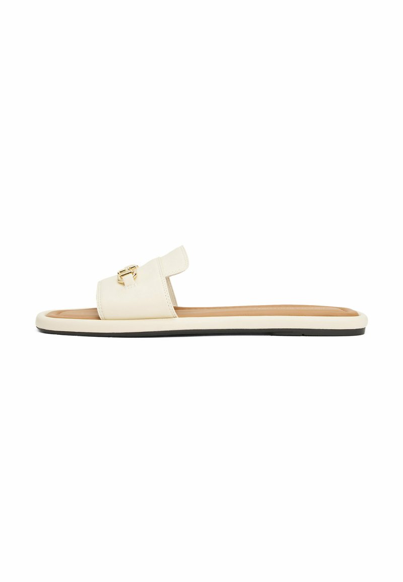 Sandalia tipo slipper en cuero crema con una cinta ancha y detalle de hebilla dorada. Suela plana con borde negro y plantilla en tono marrón para mayor comodidad.