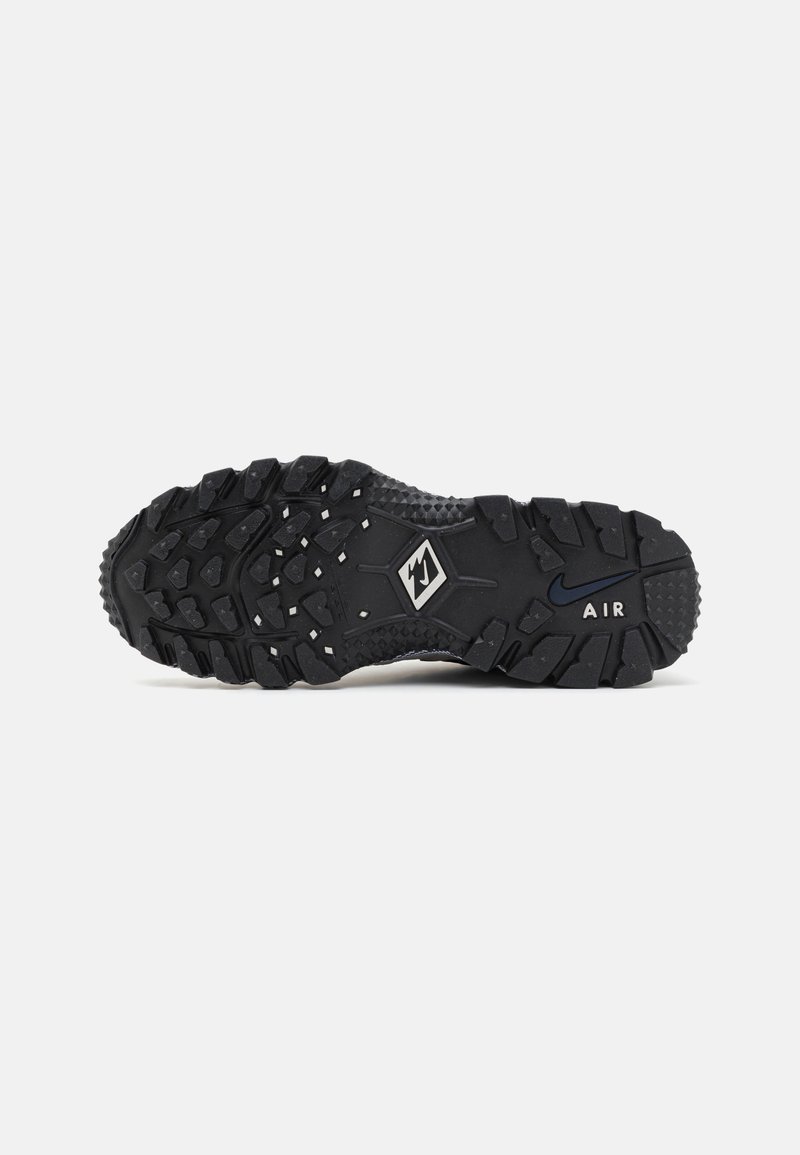 Semelle de chaussure de sport noire dotée d'un motif de relief robuste, en caoutchouc texturé, et avec des accents de logo de la marque. Les détails de traction remarquables améliorent l'adhérence.