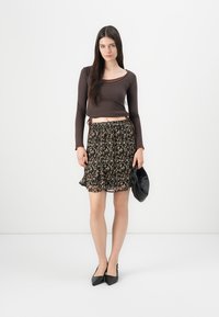 Brun, tettsittende langermet topp parret med en svart, blomstermønstret, lagdelt skjørt. Modellen holder en svart clutch og har på seg spisse svarte hæler.