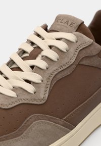 Brown suede and leather sneaker with cream laces. Features a textured overlay design and beige accents, showcasing perforated detailing.