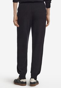 Svarta stickade byxor med avsmalnande ben, mjuk textur, elastisk midja och ribbade muddar, kombinerade med svarta och cremefärgade sneakers.