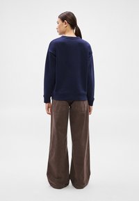 Sötétkék pulóver laza szabással és bordázott mandzsettákkal, széles szárú barna nadrággal párosítva, amely hátsó zsebekkel és puha tapintású anyaggal rendelkezik.