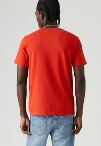 Rode katoenen T-shirt met ronde hals, korte mouwen en een rechte zoom, gedragen met lichtblauwe denim jeans met achterzakken.