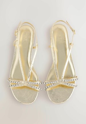 Sandales dorées avec des fines lanières, présentant une finition texturée et ornées de strass brillants sur le devant.