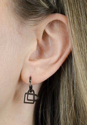 Black metal earrings feature a geometric design with overlapping squares, suspended from a simple hoop. Textured, modern aesthetic.