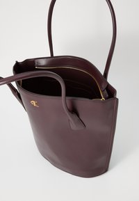 Bordeaux lederen tote bag met twee handgrepen, een ritstas in het interieur en gouden hardware accenten. Gladde textuur met een gestructureerde vorm.