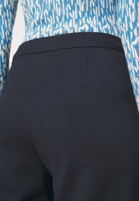 Närbild av en person som bär mörkblå byxor och en topp med blått och vitt mönster, med fokus på midje- och höftområdet.