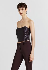 Top corto senza spalline in ecopelle burgundy con design aderente, abbinato a pantaloni su misura marrone scuro con fronte piatto e tasche laterali.