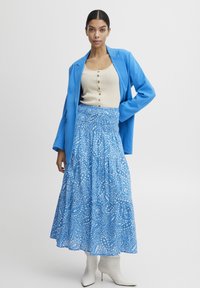Fustă maxi cu model paisley albastru, cu talie elastică, asortată cu un top ribbed bej deschis și o jachetă albastră. Purtați cu botine albe cu vârful ascuțit.
