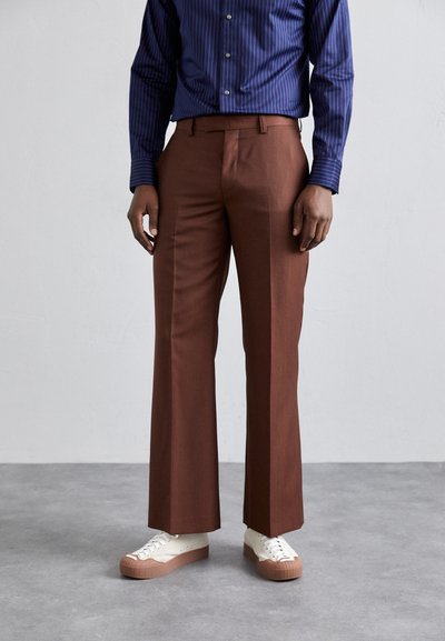 Un pantalon marron au design droit, en tissu lisse, associé à des baskets blanches avec une semelle texturée et une base en caoutchouc.