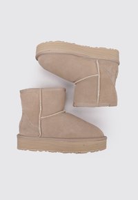 Botines de ante beige con punta redondeada, suela acanalada y costuras decorativas a lo largo de las costuras. Diseño plano con acentos mínimos.
