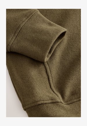 Oliivinvihreä collegepaitakangas, jossa on pehmeä ja teksturoitu pinta. Varustettu käännetyllä hihansuutaskulla ja näkyvillä ompeleilla saumoissa.