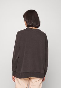 Tmavě šedá oversized mikina vyrobená z jemného materiálu, s kulatým výstřihem, spadlými rameny a volným střihem.