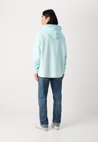 Mintgrøn hættetrøje med snørre, oversized pasform og lange ærmer, sammen med blå jeans og hvide sneakers.