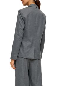 Šedý blazer z vlněné směsi s klopovým límcem, přiléhavým střihem, zadním rozparkem a jemně texturovanou látkou, doplněný o odpovídající kalhoty.