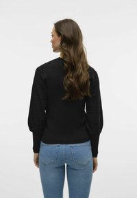 Zwarte trui met getextureerde pofmouwen en een aansluitend lichaam, gecombineerd met lichtblauwe jeans. De trui heeft een ronde hals.