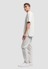 Lichtgrijze katoenen t-shirt met korte mouwen, gecombineerd met lichtgrijze denim broek en witte sneakers. Eenvoudig, recht gesneden, minimalistisch ontwerp.