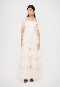 White, tiered dress with ruffled layers, short puffed sleeves, and a straight neckline. Smooth texture, flowing design, and ankle-length.