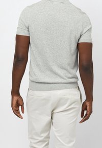 Polo gris à manches courtes avec une coupe ajustée, col et poignets côtelés, associé à un pantalon de couleur claire. Détail du tissu texturé visible.