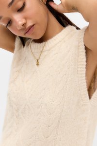 Lys beige strikket vest med kabelmønster, ærmeløst design og rund halsudskæring. Har en blød tekstur og subtile ribbede detaljer.