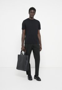 Svart bomullströja med korta ärmar, ihopparad med mörka byxor och en svart läderhandväska med texturerade vertikala sömmar.