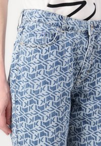 Jeans de mezclilla azul claro con un patrón geométrico en azul oscuro. Cuentan con una cinturilla, bolsillos y costuras visibles.