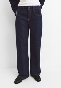 Jeans a gamba larga di un blu scuro realizzati in denim, con cuciture arancioni, chiusura a bottone, tasche frontali e una vestibilità comoda.