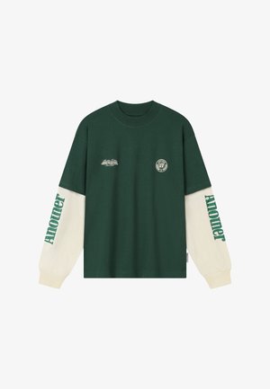 Sötétzöld hosszú ujjú ing krémszínű ujjakkal, zöld "Another" felirattal az ujjakon és kis fehér logókkal a mellrészen.