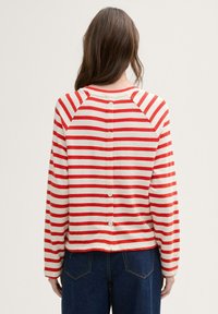Langärmliger gestreifter Pullover in Rot und Creme, mit Knopfdetail im Rücken und einem lockeren Schnitt mit Raglanärmeln.