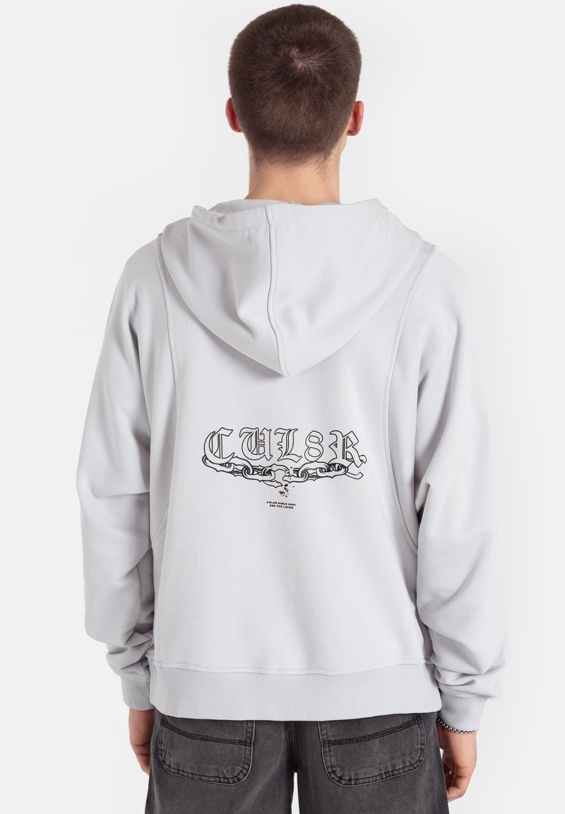 Jasnoszara bluza z kapturem i sznurkiem do regulacji, z czarnym graficznym wzorem na plecach. Wykonana z miękkiego, teksturowanego materiału, z dzianinowymi ściągaczami przy rękawach.