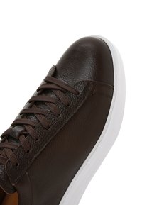 Gros plan sur une sneaker en cuir marron foncé avec des lacets marron foncé et une semelle en caoutchouc blanche.