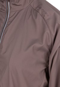 Ruskea, kevyt takki, jossa on vetoketjusuljenta, sileä pinta ja "ENDURANCE"-logo olkapäällä. Vartalonmyötäinen, slim fit -malli.