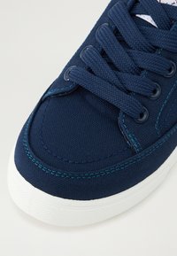 Sapatilha de lona azul-marinho com superfície texturizada, costura turquesa contrastante e sola de borracha branca, apresentando atacadores planos e ilhós.