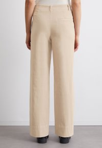 Pantalons larges beige en tissu doux, avec une taille mi-haute, une poche arrière et un ourlet soigné avec une texture lisse.