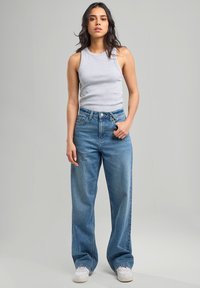 Gray sleeveless top, high-waisted light blue jeans with wide legs, and white sneakers on a plain background. Simple design with no visible patterns.