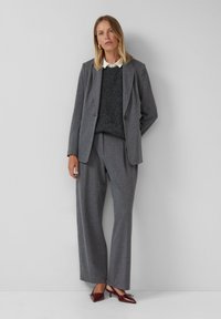 Grauer Nadelstreifenanzug mit einem zweitknöpfigen Blazer und weit geschnittenen Hosen, kombiniert mit einem dunklen Pullover und einem weißen Kragen, ergänzt durch burgunderfarbene Absatzschuhe.