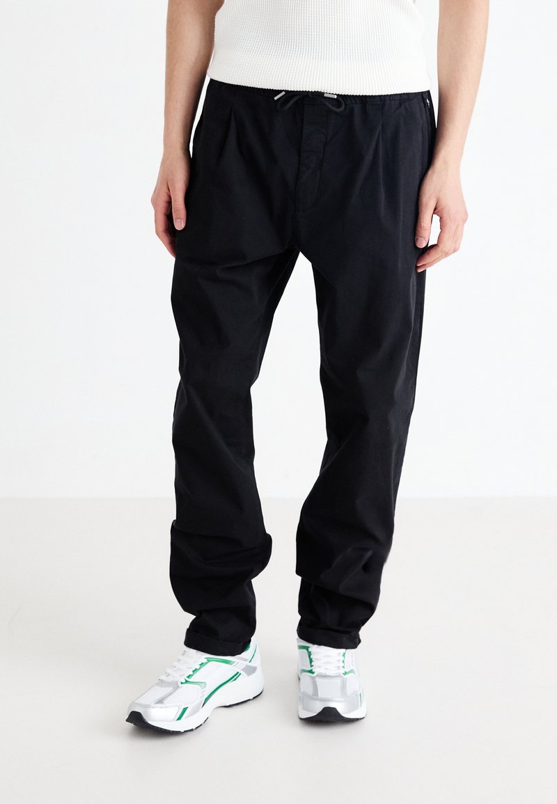 Pantalons décontractés noirs avec taille élastique et cordon de serrage. Fabriqués en tissu léger, présentant une coupe décontractée et un effilage aux chevilles.