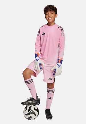 Roze keeperstrui met zwarte strepen, bijpassende shorts, kniehoge sokken en witte handschoenen met blauwe accenten, staande op een zwart-wit voetbal.