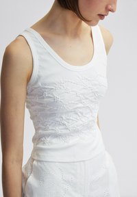Weißes ärmelloses Tanktop mit strukturierter floralem Stickerei und erhabenen Akzenten sowie einem runden Ausschnitt, hergestellt aus einem weichen Baumwollgemisch.