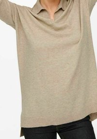 Beige pletený polo svetr s žebrovaným lemem, krátkým límečkem a bočními rozparky. Tkanina vypadá měkká a mírně strukturovaná.