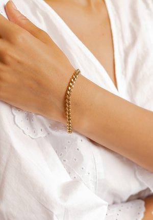 Goldene Kettenarmband mit ineinandergreifenden Gliedern, das eine glatte Oberfläche betont. Am Handgelenk getragen, kontrastiert es mit einem weißen, bestickten Stoff.