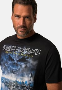 Černé bavlněné tričko s potiskem lebky a městským panoramatem, s texty "IRON MAIDEN" a "BRAVE NEW WORLD" v bílé a žluté barvě.