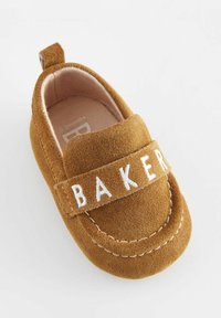 Béžové semišové detské topánočky so šitými detailmi, zaoblenou špičkou a textilným popruhom s bielou výšivkou textu "BAKER".