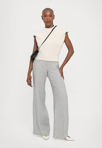 Light beige ribbed sweater with short, structured sleeves paired with wide-leg gray striped pants. Model wears a small black crossbody bag.