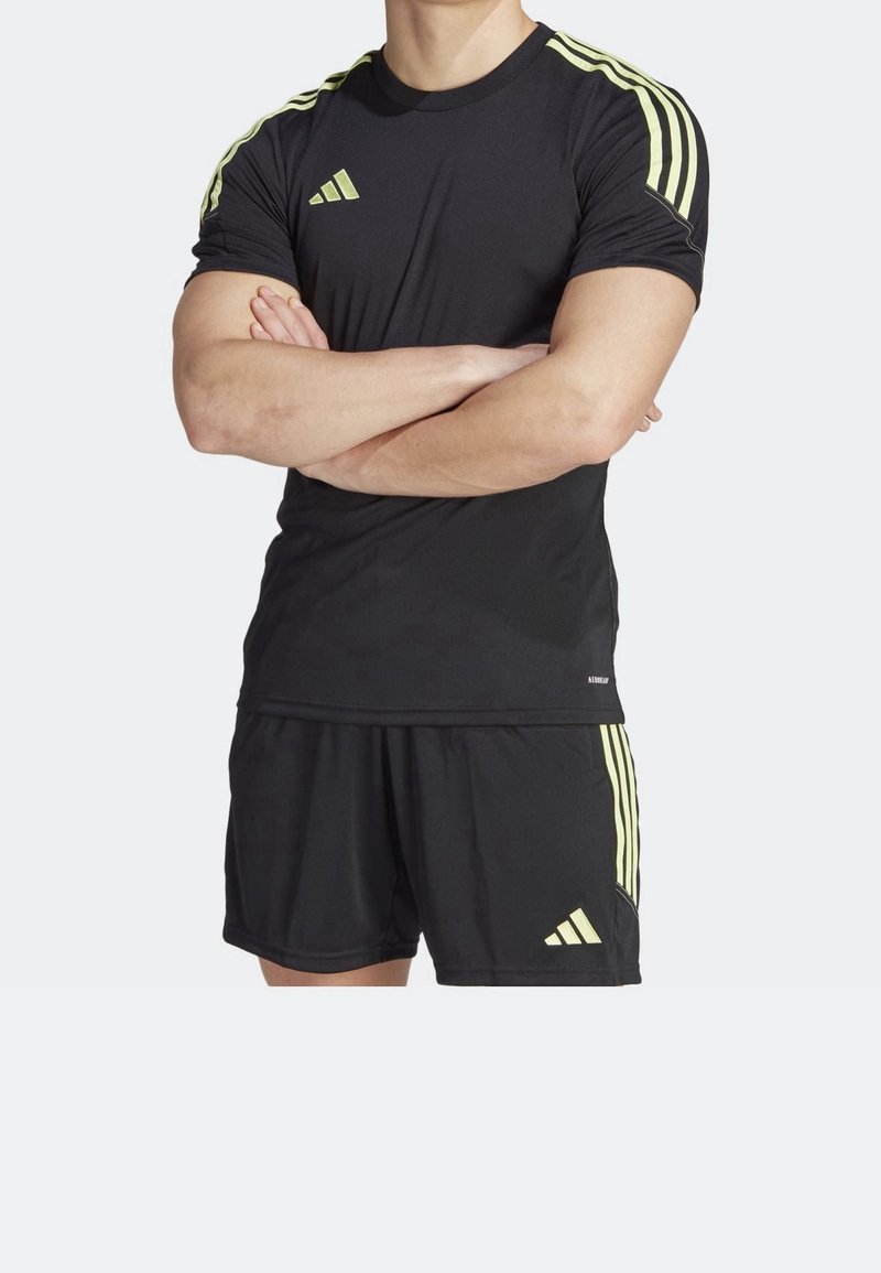 Svart kortärmad träningströja med gula ränder på axlarna och logotyp. Kombinerad med matchande svarta shorts med gula detaljer.