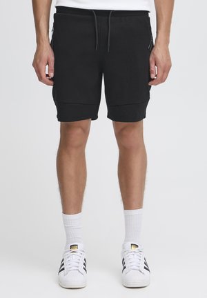 Zwarte sweatshorts met een elastische tailleband, zijzakken met rits en een gladde textuur, gecombineerd met witte sokken en zwart-witte sneakers.