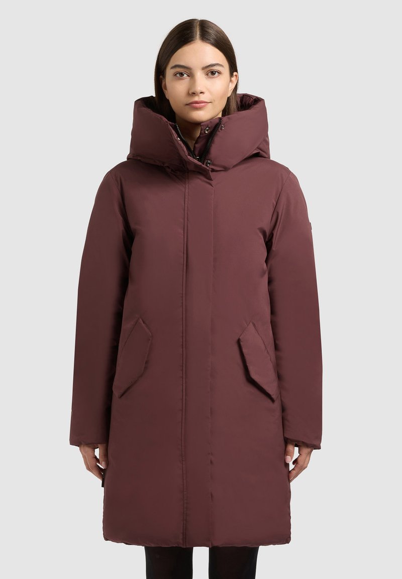 Tumepunane puffer-mantel kõrge kraega, lukuga sulgumine ja kaks esitaskut. Omab siledat tekstuuri ja põlvikuni ulatuvat disaini.