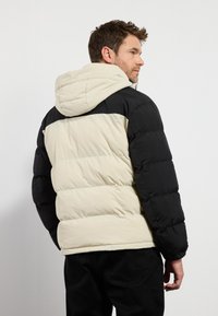 Chaqueta acolchada en negro y crema, con capucha, textura acolchada y diseño a bloques de color. Material suave e insulated para el calor.