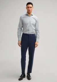 Camicia azzurra a fantasia con maniche lunghe abbinata a pantaloni eleganti blu navy e scarpe da uomo nere. Tessuto con una texture liscia.