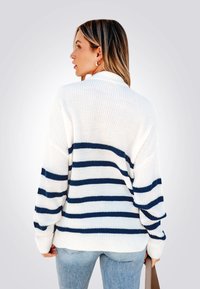 Suéter blanco de punto con rayas horizontales azules, corte relajado, puños acanalados y dobladillo dividido. Combinado con jeans de mezclilla azul claros.